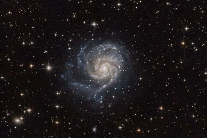 Galassia a spirale con nucleo luminoso, bracci stellari visibili e campo di stelle nel cosmo profondo.